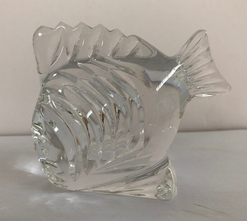 Peut inclure: Une sculpture de poisson en verre transparent avec un design textur&eacute; d&eacute;taill&eacute;. Le poisson est tourn&eacute; vers la gauche et a une nageoire sur le dos et une nageoire caudale.