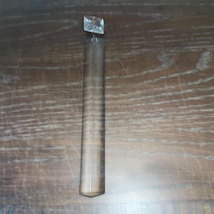 May include: A clear crystal prism with a square top and a long, rectangular body. The prism is hanging from a string.