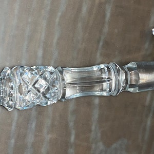 May include: A clear, cut-glass gavel with a decorative handle and head. The handle features diamond and geometric patterns, and the head has a rectangular shape. The gavel is designed for ceremonial use.