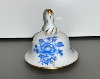May include: White porcelain bell with a blue and gold floral design. The bell has a gold knob on top.