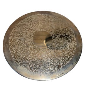 以下が含まれることがあります： 銀色の丸い金属製のトレイで、表面には複雑な花柄とスクロールワークのデザインがエッチングされています。トレイの中央には円形の開口部があり、縁はわずかに盛り上がっています。デザインは対称的で詳細です。