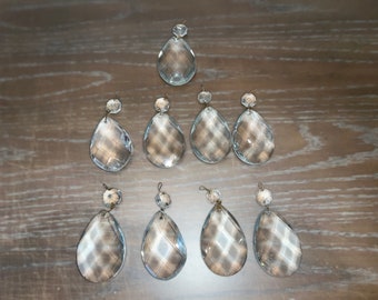 May include: A set of ten clear glass crystal teardrop pendants with a faceted design. The pendants are strung on a silver wire and have a small loop at the top for hanging.