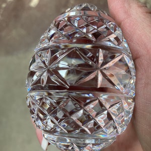 K&ouml;nnte beinhalten: Ein klarer, eif&ouml;rmiger Dekorationsgegenstand aus geschliffenem Glas. Das Ei weist ein detailliertes geometrisches Muster aus Rauten und Sternen auf. Die Facetten fangen das Licht ein und erzeugen einen funkelnden Effekt. Es ist wahrscheinlich ein Dekorationsartikel.