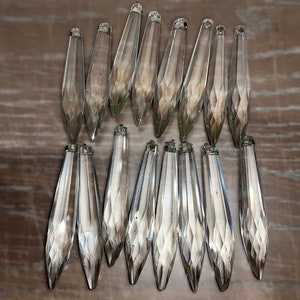 May include: A set of 18 clear crystal teardrop-shaped prisms. The prisms are faceted and have a pointed tip. They are arranged in two rows of nine.