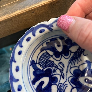May include: A small, white ceramic bowl with a blue and white floral design. The bowl has a scalloped edge and a blue rim.