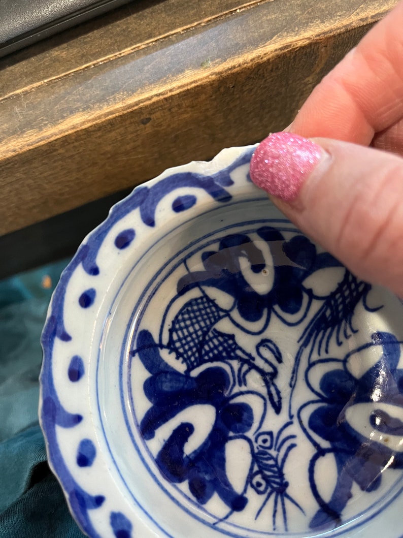 May include: A small, white ceramic bowl with a blue and white floral design. The bowl has a scalloped edge and a blue rim.