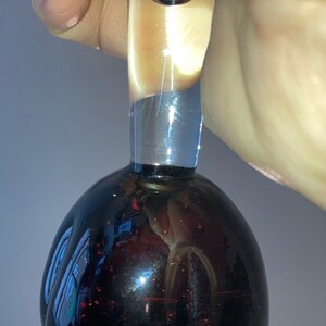 May include: A clear glass bottle stopper with a black, round, and reflective base. The stopper has a long, clear neck.