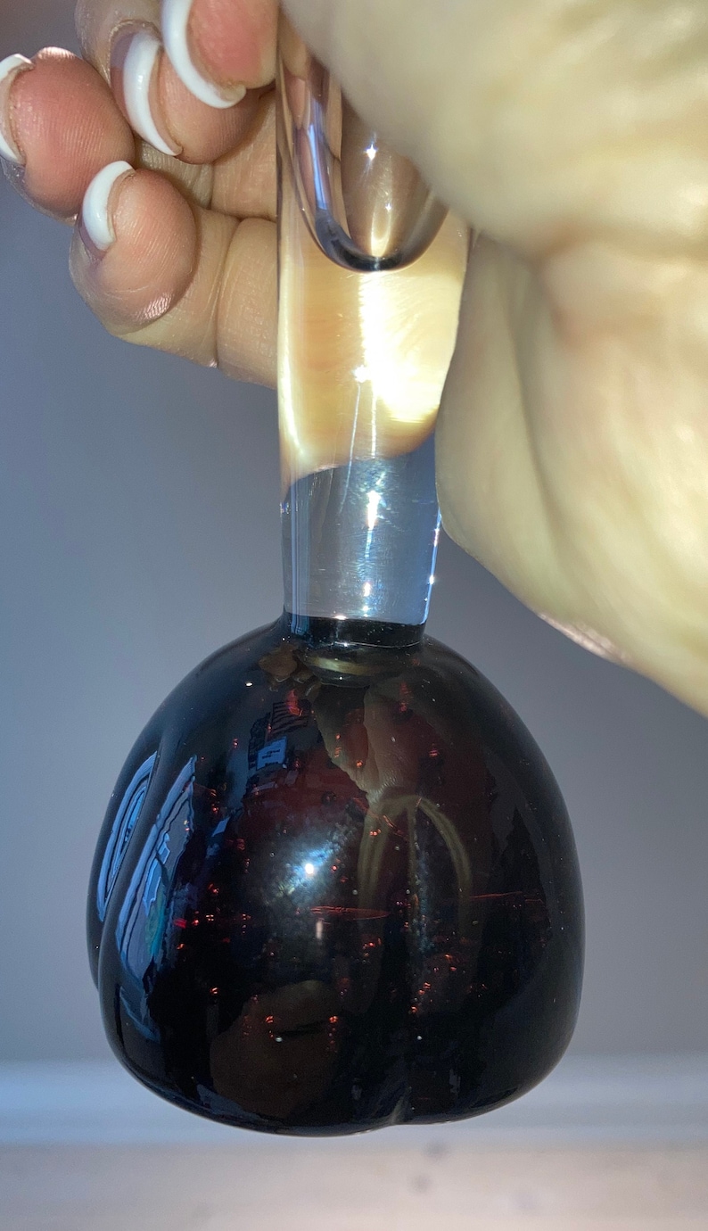 May include: A clear glass bottle stopper with a black, round, and reflective base. The stopper has a long, clear neck.