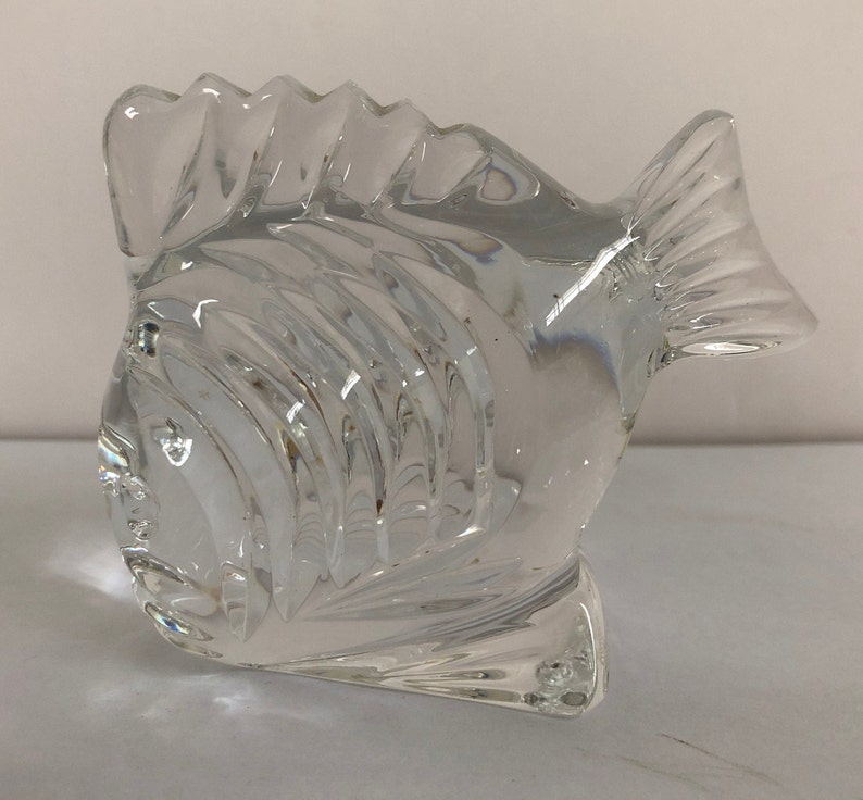 Peut inclure: Une sculpture de poisson en verre transparent avec un design textur&eacute; d&eacute;taill&eacute;. Le poisson est tourn&eacute; vers la droite et a un corps l&eacute;g&egrave;rement incurv&eacute;.
