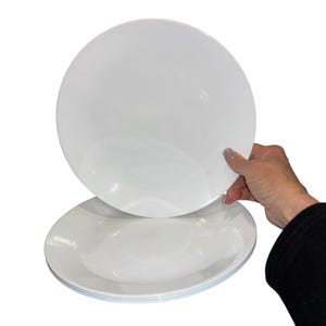Puede incluir: Una pila de platos redondos blancos. Una mano levanta un plato, revelando la pila de platos de abajo. Los platos tienen un diseño sencillo y limpio, perfecto para el uso diario. Los platos están hechos de un material duradero.