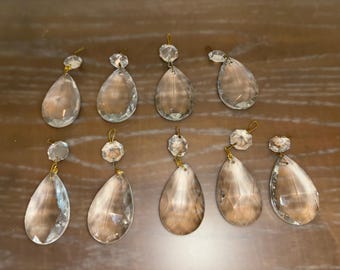 May include: Ten clear glass teardrop-shaped crystal prisms with gold-colored metal accents. The prisms are hanging from a gold-colored metal loop.