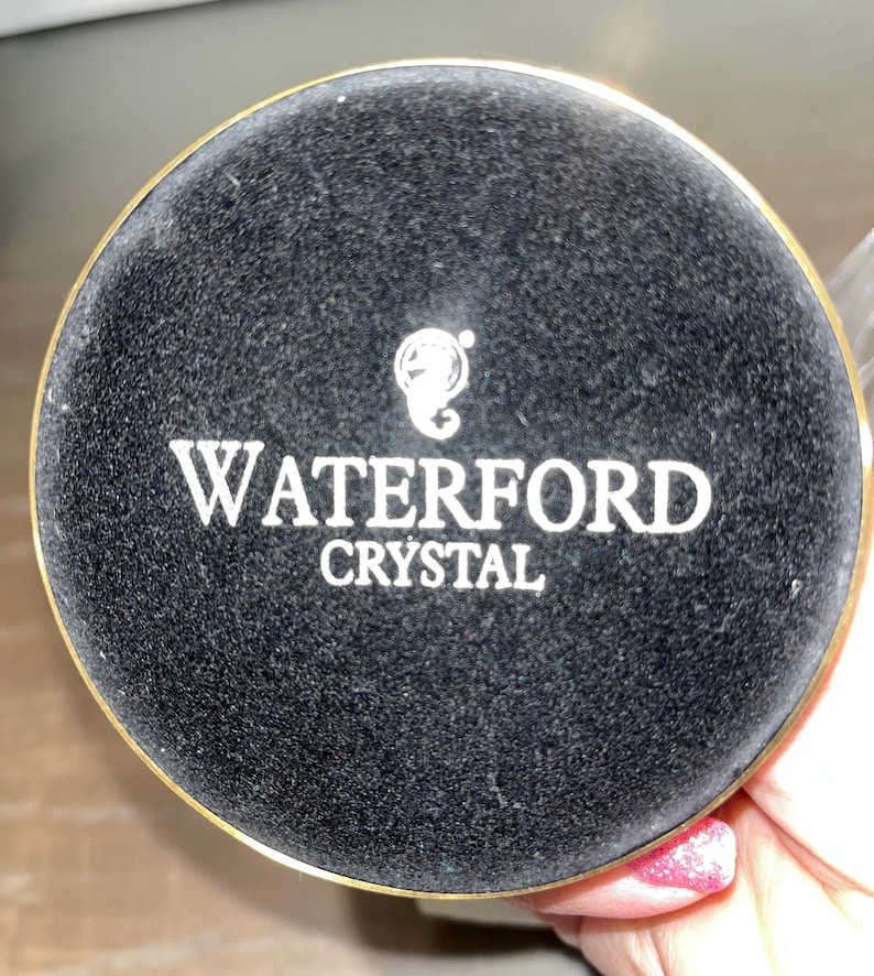 May include: A black circular base with a gold rim and the text "WATERFORD CRYSTAL" in white lettering.