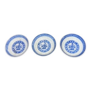 May include: Three small, round, white porcelain dishes with blue floral designs. Each dish has a blue border with a geometric pattern and a central floral motif. The dishes are arranged at slightly different angles.