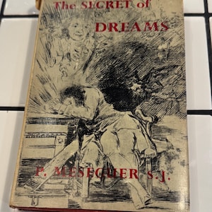 Puede incluir: Libro antiguo titulado "The Secret of Dreams" con una cubierta desgastada. La ilustraci&oacute;n de la portada muestra a una persona apoyada en una mesa, con otras figuras y texto rojo. El t&iacute;tulo del libro y el nombre del autor son visibles.