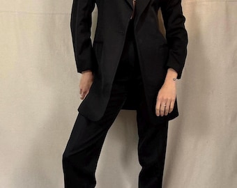 May include: A black suit consisting of a blazer and matching trousers. The blazer has a classic lapel and a single-button closure. The trousers are straight-legged. The outfit is worn over a white top.