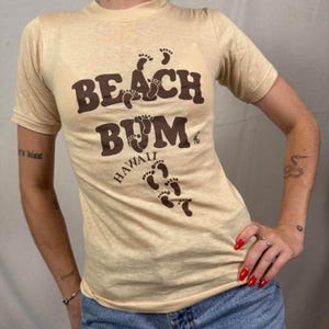 May include: A white ceramic mug with a black handle and the text "But First, Coffee" in a bold, black font. The mug is set against a blurred background, suggesting a cozy setting.