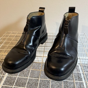 Könnte beinhalten: Ein Paar schwarze Lederstiefel mit Reißverschluss an der Vorderseite. Die Stiefel haben eine abgerundete Spitze und einen niedrigen Absatz.