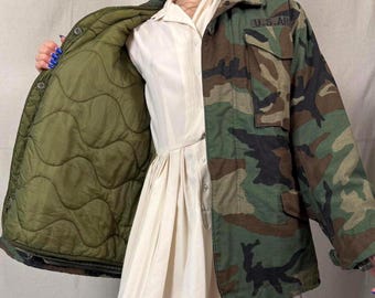 May include: Camouflage print jacket with a green quilted lining. The jacket features a button-up front, two chest pockets, and the text "U.S. AR" on the right side. The jacket is a mix of green, brown, and black.