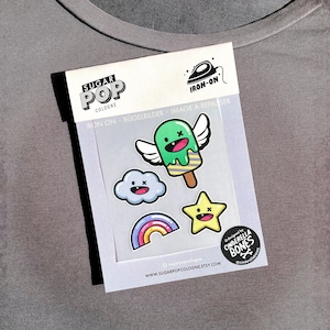 May include: A set of five iron-on patches featuring a green popsicle with wings, a blue cloud, a rainbow, a yellow star, and a black and white logo that says "Cinderella Bones". The patches are designed for clothing and other fabric items.