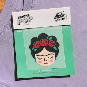 Könnte beinhalten: Bügeleisen-Patch mit einer farbenfrohen Illustration von Frida Kahlo mit einer Blumenkrone. Der Patch befindet sich auf einem weißen Hintergrund mit dem Text "Sugar Pop Cologne" und "Iron-on" in Schwarz.
