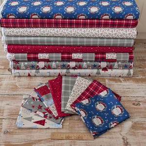 May include: A collection of folded and rolled fabric bolts featuring various Christmas-themed patterns including Santa Claus, holly, stars, and plaid designs in red, blue, grey, and white. A wooden ruler is placed at the bottom for scale.
