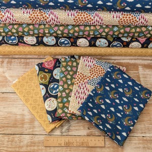 Könnte beinhalten: Eine Sammlung von Stoffstücken mit Mustern in verschiedenen Farben, darunter Blau, Gold und Grün. Die Stoffe zeigen Designs wie Monde, Wolken, Blumen und Stickrahmen. Unten befindet sich ein Lineal von The Fabric Squirrel.