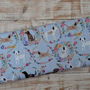 May include: A roll of light blue fabric with a repeating pattern of dogs and floral wreaths. The dogs are in brown, black, and white. The fabric has the text "EVERY HOME Every Dog" printed on the edge.