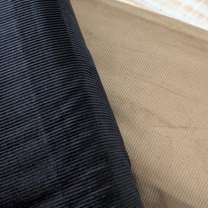 May include: Close-up of two fabric swatches. One is black corduroy, and the other is tan corduroy. The fabrics have a ribbed texture, and the image highlights the contrast between the colors and textures.