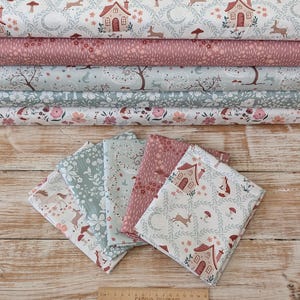 May include: A collection of five folded fabric swatches and five stacked fabric bolts featuring woodland patterns with houses, foxes, rabbits, mushrooms, and floral motifs in muted tones. A wooden ruler shows a length of 38 cm at the bottom.