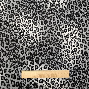 May include: Black and white animal print fabric with a subtle shimmer. The fabric has a repeating pattern of leopard spots.