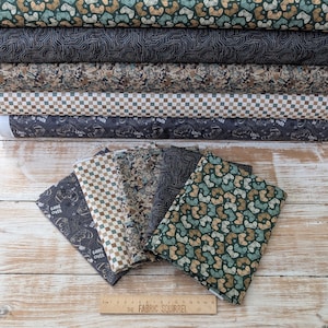 May include: An assortment of fabric rolls and folded fabric pieces featuring diverse patterns. Designs include video game controllers, circuit board patterns, and checkered patterns in shades of green, brown, and grey. Some fabrics have the text "GAME OVER" and "LEVEL UP".
