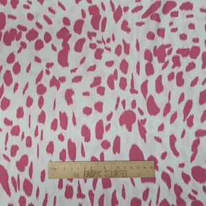 May include: White fabric featuring a repeating pattern of pink, irregular shapes. A wooden ruler with the text "THE FABRIC SQUIRREL" is placed across the fabric. The ruler measures up to 15 cm.