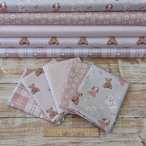 May include: A selection of pink and grey fabric rolls and folded pieces. The fabrics display patterns of teddy bears, dolls, bunnies, crosses, and hearts. The text "THE FABRIC SQUIRREL" is visible on a ruler.