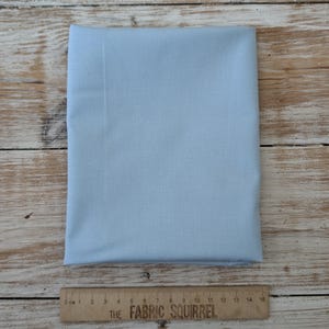 Könnte beinhalten: Ein hellblauer Stoffmuster, 38 cm lang, liegt auf einer Holzoberfläche.