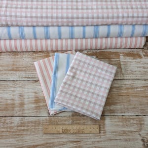 May include: Three fabric swatches in pink and white gingham, blue and white stripes, and pink and white stripes. The swatches are laid out on a wooden surface with a ruler labelled "The Fabric Squirrel" in the foreground.