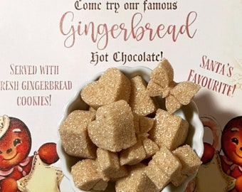 May include: A white bowl filled with heart-shaped brown sugar cubes. The bowl is on a pink and white background with the text "Come try our famous Gingerbread Hot Chocolate!" and "SANTA'S FAVORITE!"