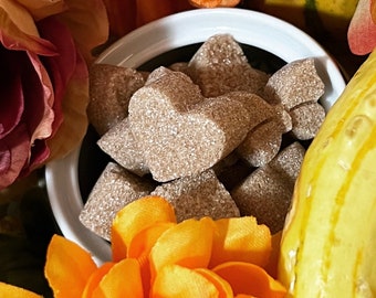 May include: A white bowl filled with brown sugar cubes, surrounded by orange and yellow flowers. The sugar cubes are in the shape of hearts.