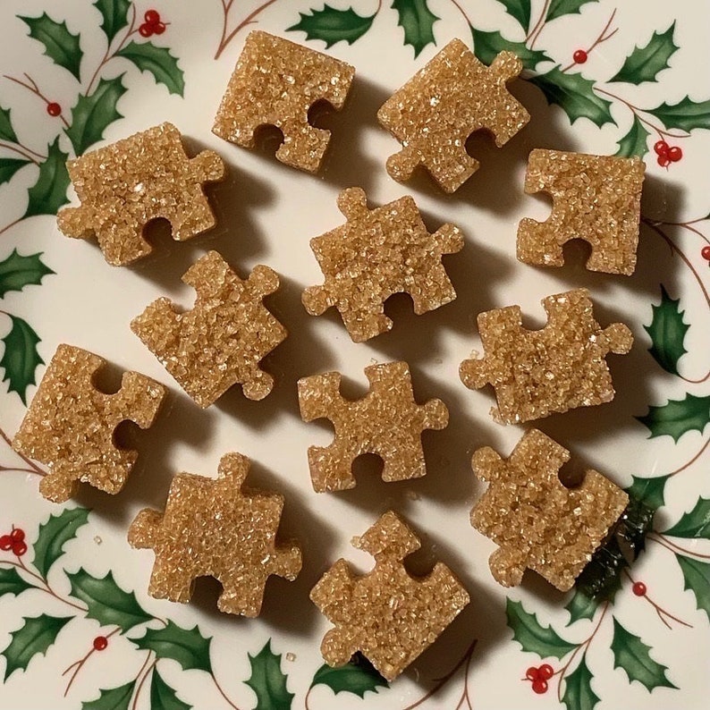 Może przedstawiać: Talerz z zielonym i białym wzorem ostrokrzewu przedstawia 12 brązowych cukrowych puzzli. Elementy układanki są ułożone w losowy spos&oacute;b na talerzu.