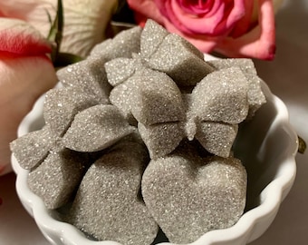 May include: A white bowl filled with sugar cubes shaped like butterflies and hearts. The sugar cubes are covered in a sparkly, glittery coating.
