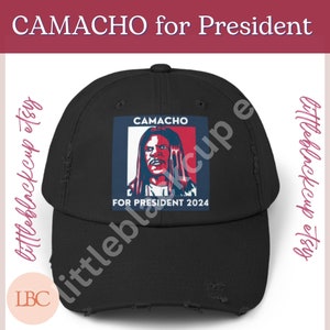 Puede incluir: Gorra de béisbol negra desgastada con un gráfico blanco, rojo y azul de un hombre con el texto "CAMACHO FOR PRESIDENT 2024".