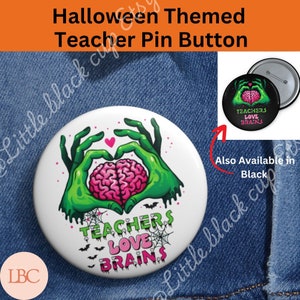 Può includere: Un bottone bianco con una mano di zombie verde che tiene un cervello rosa a forma di cuore. Il testo "Teachers Love Brains" è scritto sotto le mani. Il bottone è su uno sfondo di jeans blu.