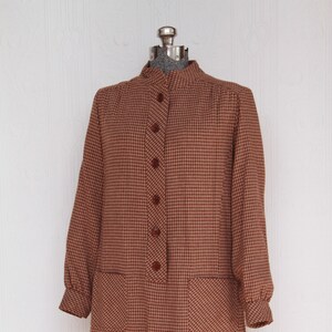 May include: A brown and beige gingham dress with a high collar and long sleeves. The dress has a button-up front and two patch pockets.
