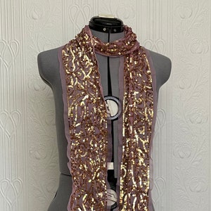 May include: A pink and gold sequined scarf with a floral pattern. The scarf is draped over a mannequin.