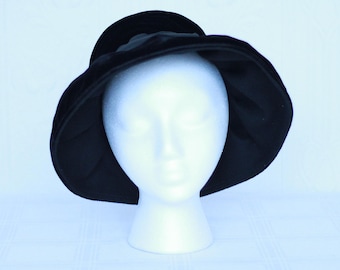 May include: A black velvet hat with a wide brim. The hat is sitting on a white mannequin head.