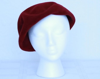 May include: A burgundy velvet beret hat on a white mannequin head.