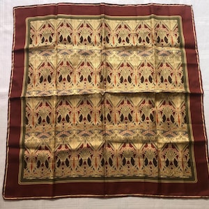 May include: A square silk scarf with an Art Nouveau floral pattern in gold, red, and brown. The scarf has a dark burgundy border and the word "LIBERTY" is visible in the corner.