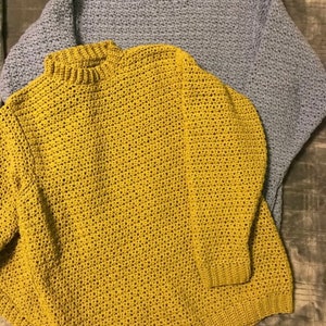 May include: Two crocheted sweaters, one in a mustard yellow color and the other in a light blue color. Both sweaters have a high neck.