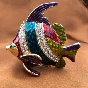 May include: A colorful metal fish figurine with a purple, green, red, and yellow striped design. The fish is decorated with clear rhinestones and has a gold finish.