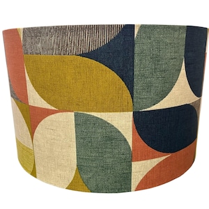 May include: A cylindrical drum lampshade featuring a repeating geometric pattern of semi-circles and quarter-circles. The fabric displays a textured weave in a colour palette of mustard yellow, navy blue, sage green, terracotta orange, and cream.