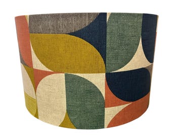 Può includere: Un paralume cilindrico caratterizzato da un motivo geometrico ripetuto di semicerchi e quarti di cerchio. Il tessuto presenta una trama testurizzata in una palette di colori giallo senape, blu navy, verde salvia, arancione terracotta e crema.